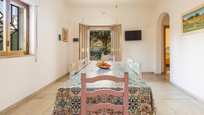 A dining area with a long table, chairs, and a bowl of fruit. - 2679 Villetta Filomena - Appartamento Leo by Barbarhouse (Manduria)