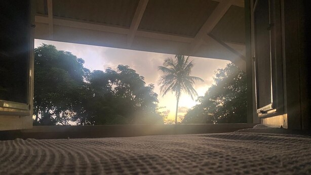 Een kamer met een groot raam met uitzicht op een zonsondergang en palmbomen.