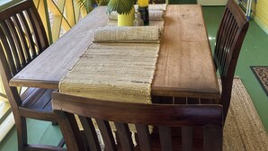 Een houten eettafel met geweven tafelonderleggers, stoelen en een potplant.