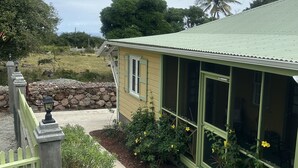 Een geel gebouw met een groen dak, omgeven door een tuin met gele bloemen en een stenen muur.
