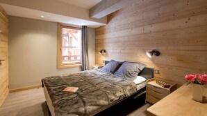 A bedroom with a bed, bedside tables, a nightstand, a lamp, and a vase with flowers. - Bain À Remous Privé! Chalet au coeur du Village (L'Alpe d'Huez)