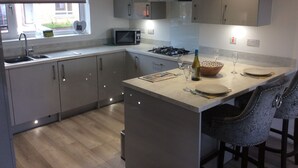 Een moderne keuken met grijze kastjes, een magnetron, een gasfornuis en een eethoek met barstoelen.