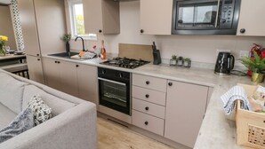 A modern kitchen with a built-in oven, microwave, and gas stove. There is a dining area with a sofa and a small table. - Plot 18 Meadow View (Morpeth)
