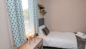 A bedroom with a bed, bedside table, lamp, and curtains. - Plot 18 Meadow View (Morpeth)