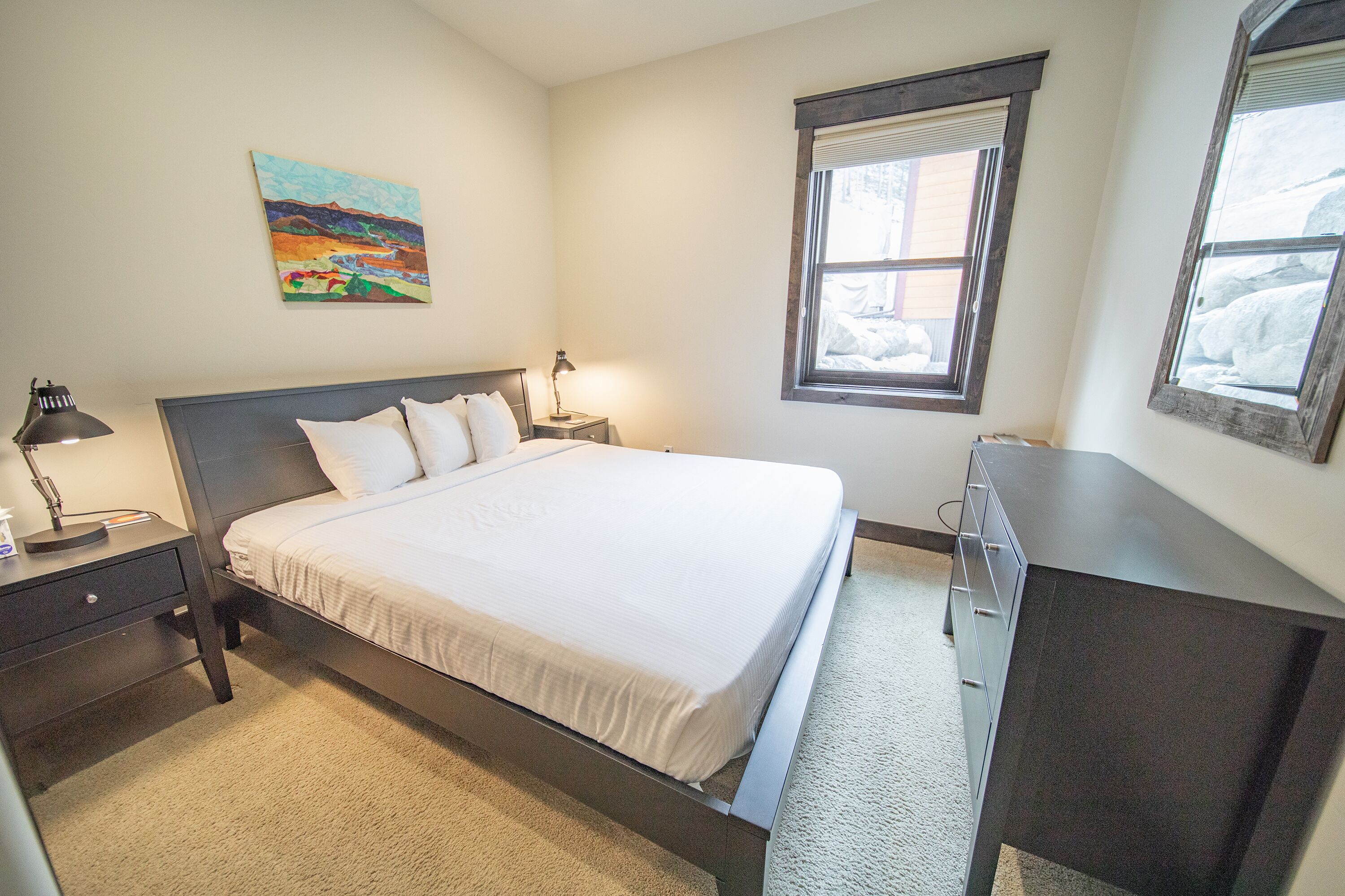 Une chambre à coucher avec un lit, des tables de chevet, une commode, un tableau et une fenêtre.