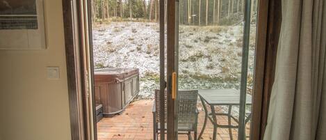 A sliding glass door leading to an outdoor patio with a wooden deck, a hot tub, and a table and chairs.