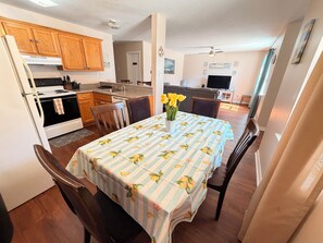 Un comedor con una mesa dispuesta para cuatro, una cocina con armarios de madera y una sala de estar con televisor.