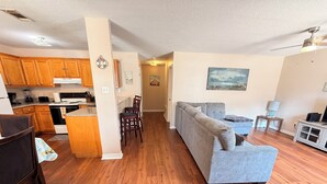 A modern living room with a grey sofa, wooden flooring, and a kitchen area with wooden cabinets and appliances. - ENTIRE Place 2 Bed 2 Bath. Everything You Need for a Hassle-Free Stay in Biloxi. (Biloxi)