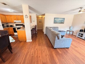 Ein modernes Wohnzimmer mit grauem Sofa, Holzboden und einer Küchenzeile mit Holzschränken und Geräten.