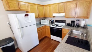 A compact kitchen with wooden cabinets, a white refrigerator, a microwave, a stove, and a sink. - ENTIRE Place 2 Bed 2 Bath. Everything You Need for a Hassle-Free Stay in Biloxi. (Biloxi)