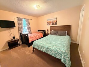 A bedroom with a bed, a TV, a bedside table, and a window with curtains.