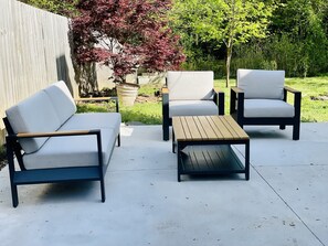 An outdoor patio with a sofa, two armchairs, and a wooden table. - Cozy Guilford Hills Retreat (Greensboro)