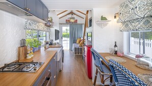 A compact kitchen with a stove, sink, and a dining area with a bench. - New Tiny House (Camp Hill)