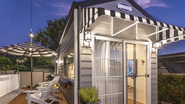 A small, single-story building with a covered patio area, a grill, and outdoor seating. - New Tiny House (Camp Hill)