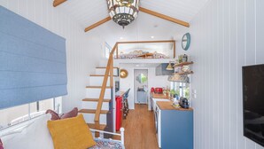 A compact, open-plan living space with a loft bedroom, a kitchen area, and a dining area. - New Tiny House (Camp Hill)