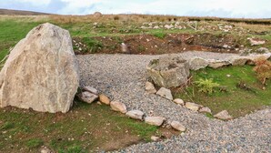 A natural outdoor setting with a large rock formation, a gravel path, and a metal container.