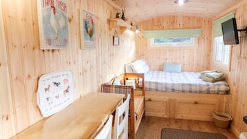 A cozy cabin with a wooden interior, a bed with a plaid bedspread, a small desk, and a window with a view of greenery.