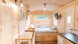 A cozy cabin with a wooden interior, a bed with a plaid blanket, a dining table, and a small kitchen area.