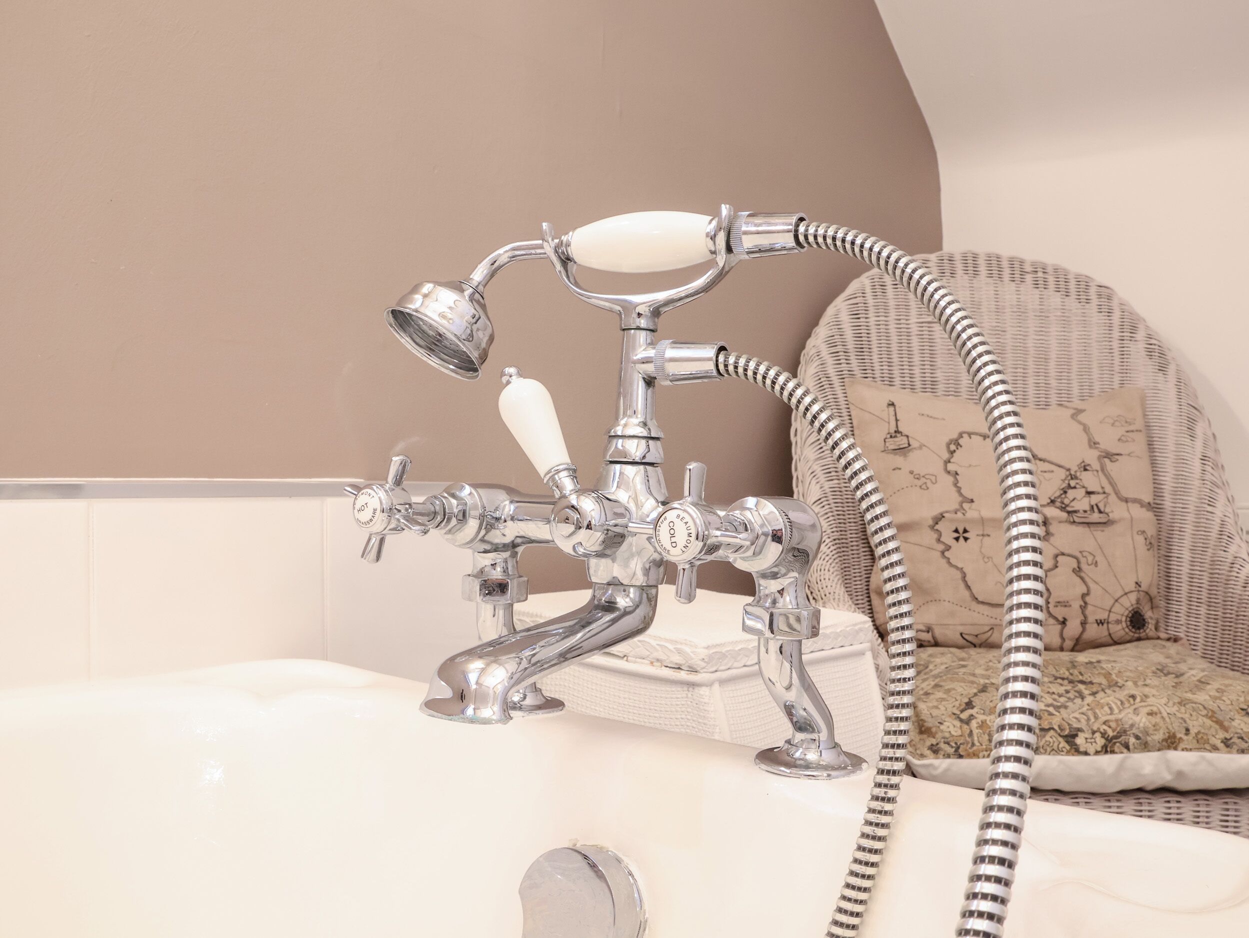 Un baño con ducha de estilo vintage, una bañera blanca y un sillón de mimbre con diseño de mapa.