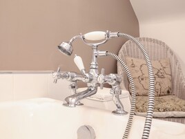 Un baño con ducha de estilo vintage, una bañera blanca y un sillón de mimbre con diseño de mapa.