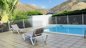 A swimming pool with two lounge chairs, a tiled deck, a white fence, and a mountainous backdrop. - Small sugar bowl duplex with sea view (Cul de Sac)
