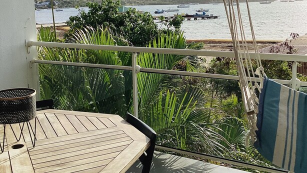 A wooden table and chairs on a balcony with a view of boats on the water and greenery in the background. - Small sugar bowl duplex with sea view (Cul de Sac)