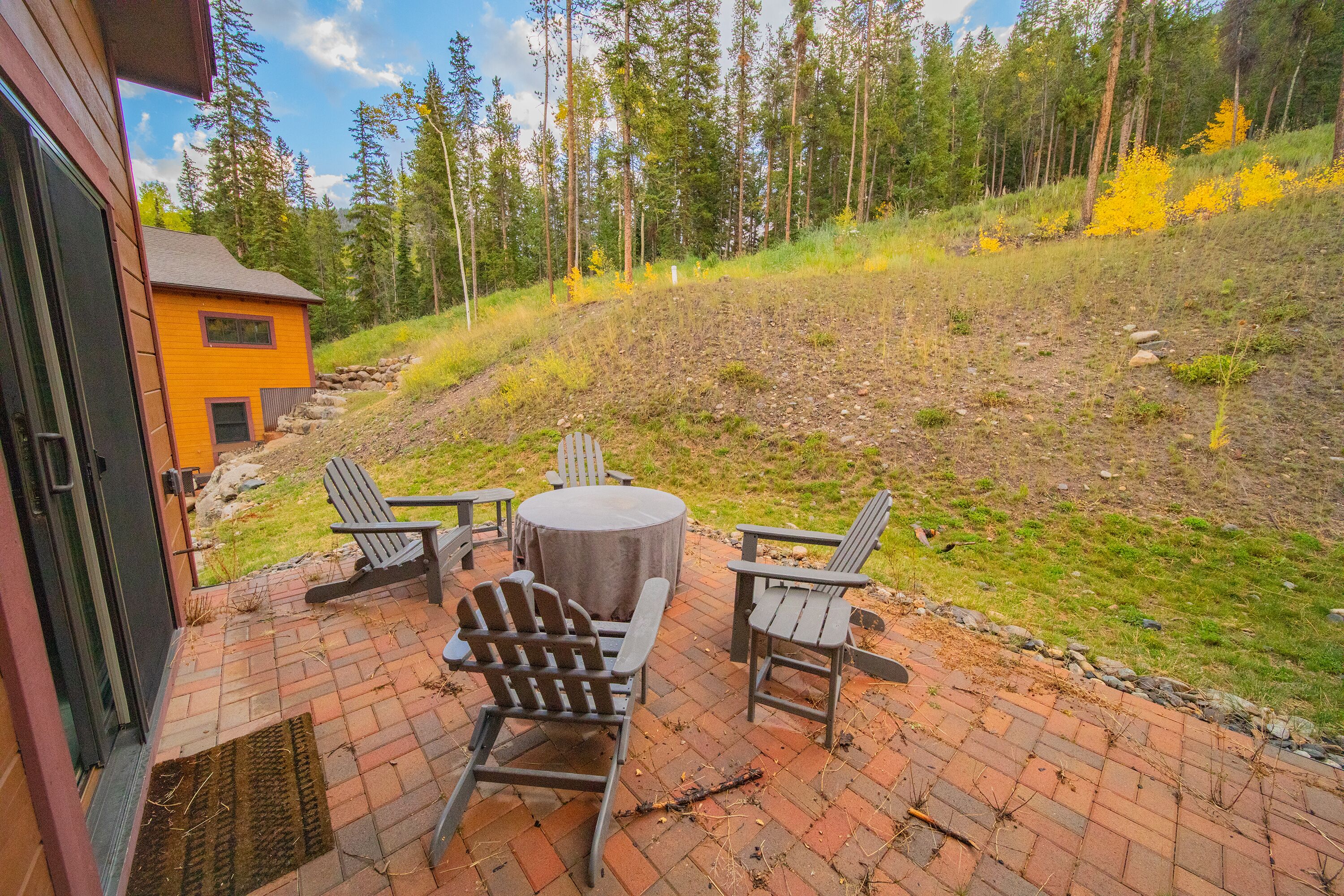 An outdoor patio with a brick floor, a round table, and Adirondack chairs.