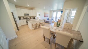 A modern kitchen with white cabinets, a central island with stools, and a dining area with a wooden table and chairs. - Clearwater Lofts Bldg 1 303 (Keystone)