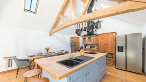 A modern kitchen with wooden beams, a central island, bar stools, a stainless steel refrigerator, and wooden cabinets. - Swallow Barn (Cockermouth)