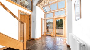 A spacious hallway with a stone floor, wooden doors, and a view of the outdoors through large windows. - Swallow Barn (Cockermouth)