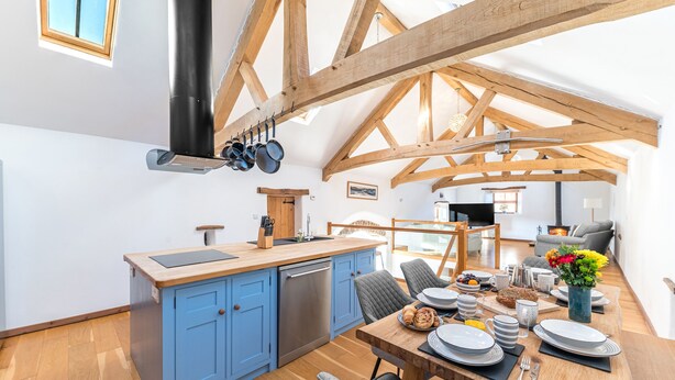 A modern kitchen with blue cabinets, wooden beams, and a dining area with a wooden table and chairs. - Swallow Barn (Cockermouth)