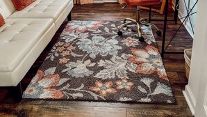Un salón acogedor con un sofá blanco, un sillón rojo, una alfombra estampada y una mesa de comedor con una lámpara.