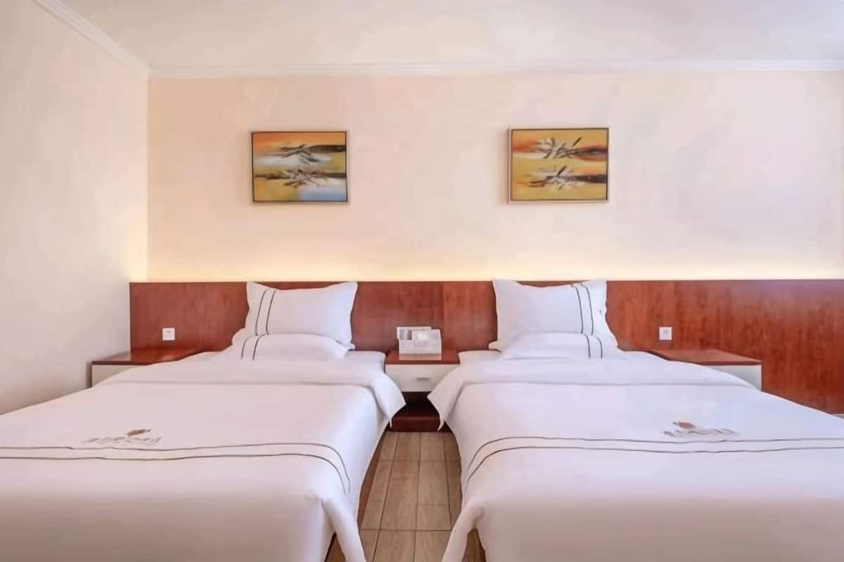 A hotel room with two beds, wooden headboards, artwork on the walls, and a nightstand with a phone.