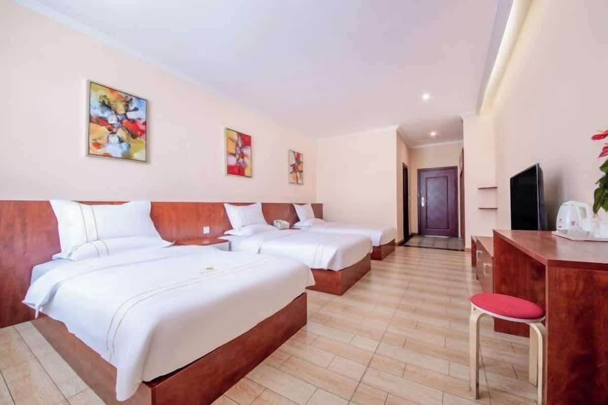 A hotel room with three beds, a desk with a chair, and artwork on the walls.