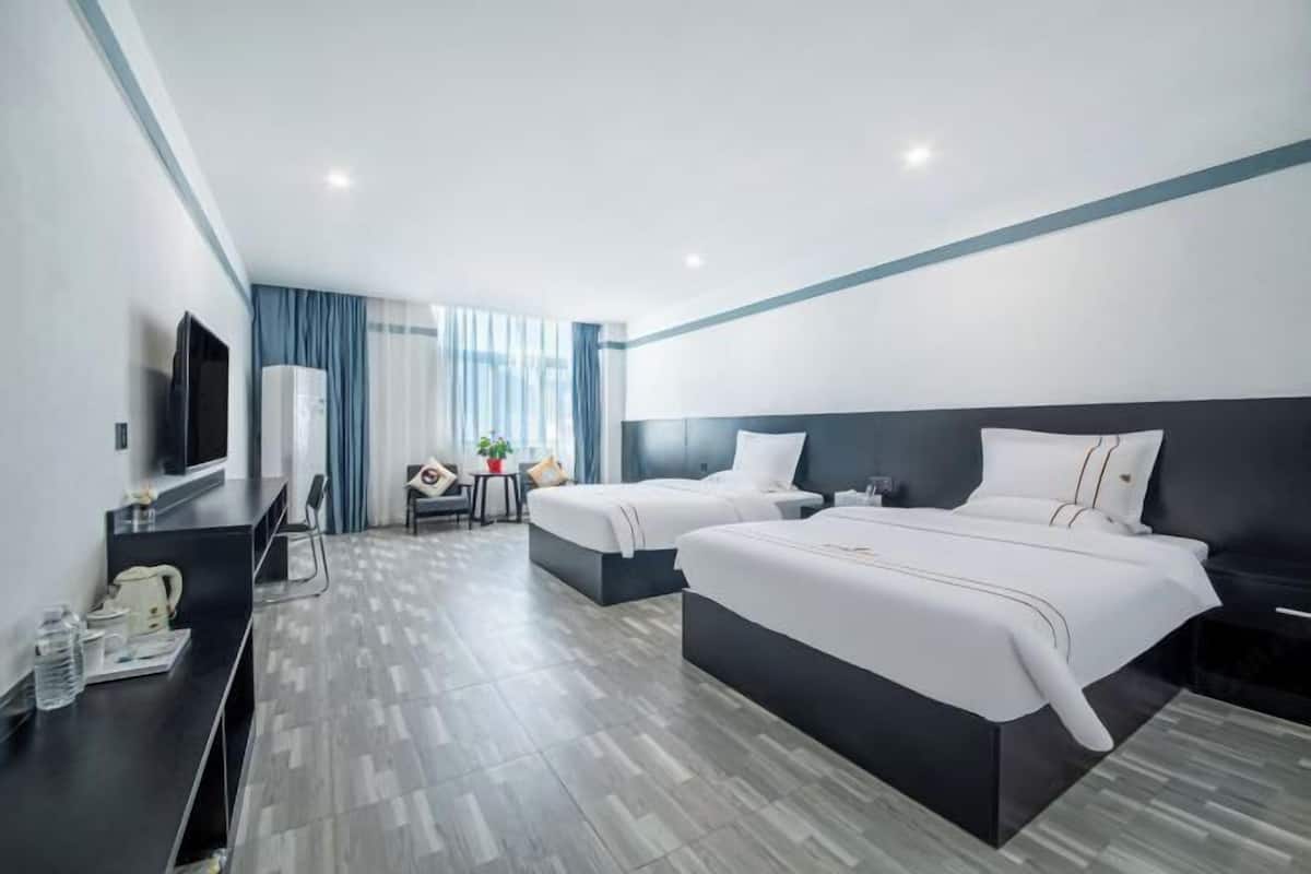 A modern hotel room with two beds, a desk with a TV, and a small seating area.
