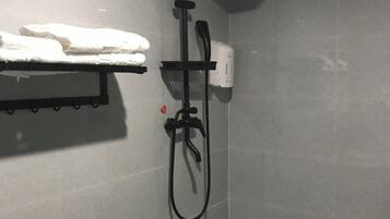 Zona de ducha con cabezal de ducha de mano, un perchero con toalla doblada y dispensador de jabón en la pared.