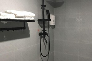 Zona de ducha con cabezal de ducha de mano, un perchero con toalla doblada y dispensador de jabón en la pared.