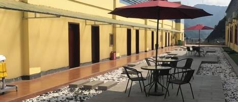 An outdoor patio with tables and chairs, a yellow building, and red umbrellas.