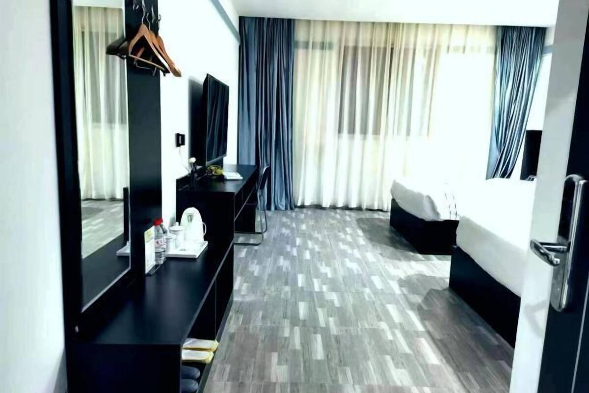 A hotel room with a bed, a desk with a mirror, a television, and a window with curtains.