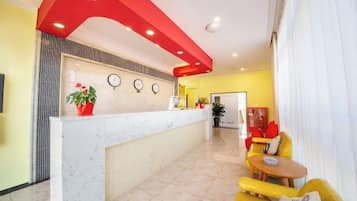 A reception area with a marble counter, a clock, and a plant. There are yellow sofas and a small table.