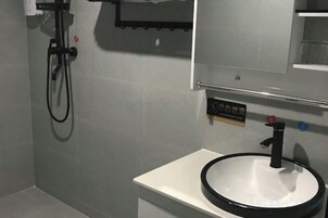 Un baño con un lavamanos blanco, un espejo y un cabezal de ducha.