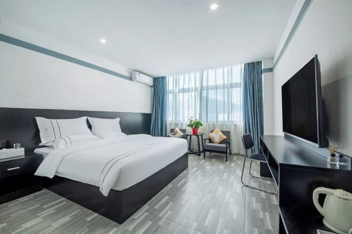A modern hotel room with a large bed, a desk, a television, and a window with curtains.