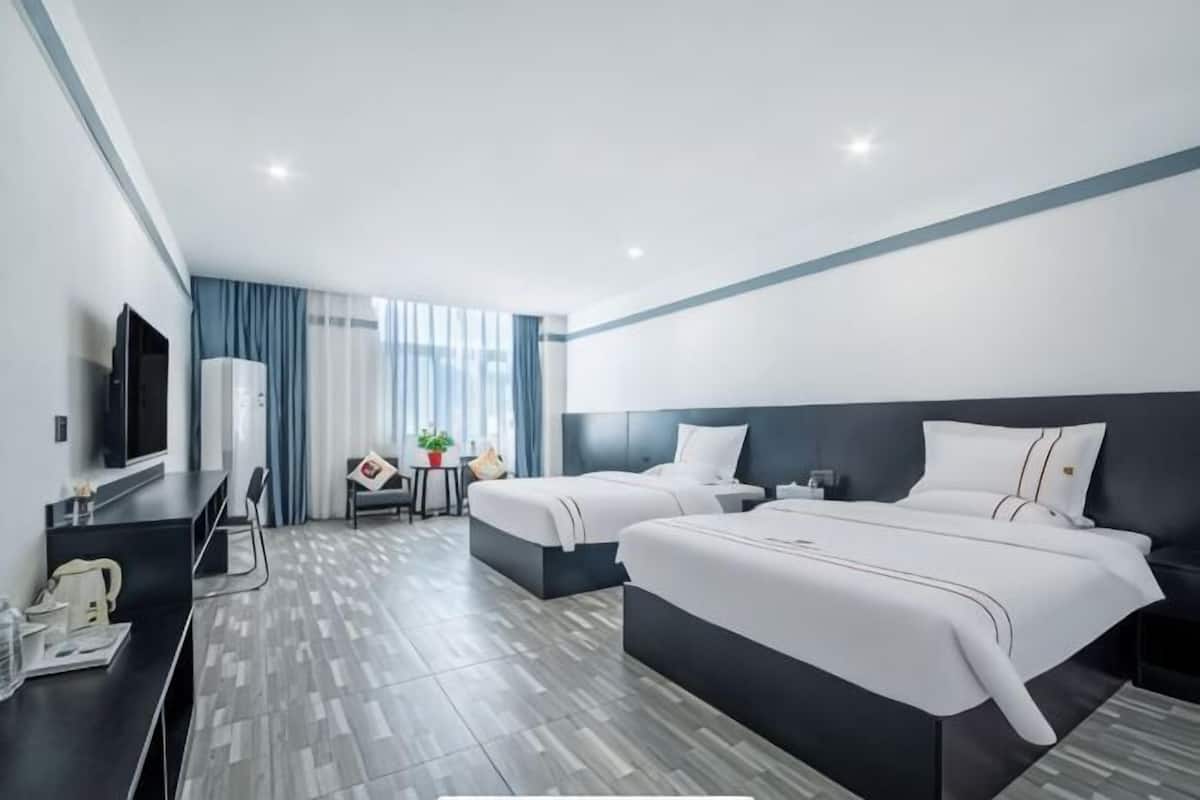 A modern hotel room with two beds, a desk, a chair, a TV, and a window with curtains.
