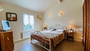 A bedroom with a bed, bedside lamps, a TV on a wooden cabinet, a window, and decorative wall lights. - Pretty villa close to beaches and cycle paths (LA COUARDE SUR MER)