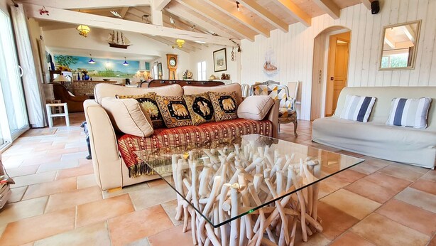 A spacious living room with a sofa, a glass coffee table, and a white couch. There is a kitchen area in the background with a dining table and chairs. - Pretty villa close to beaches and cycle paths (LA COUARDE SUR MER)
