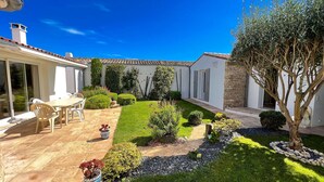 A patio with a table and chairs, surrounded by a well-maintained garden with various plants and a stone pathway. - Pretty villa close to beaches and cycle paths (LA COUARDE SUR MER)