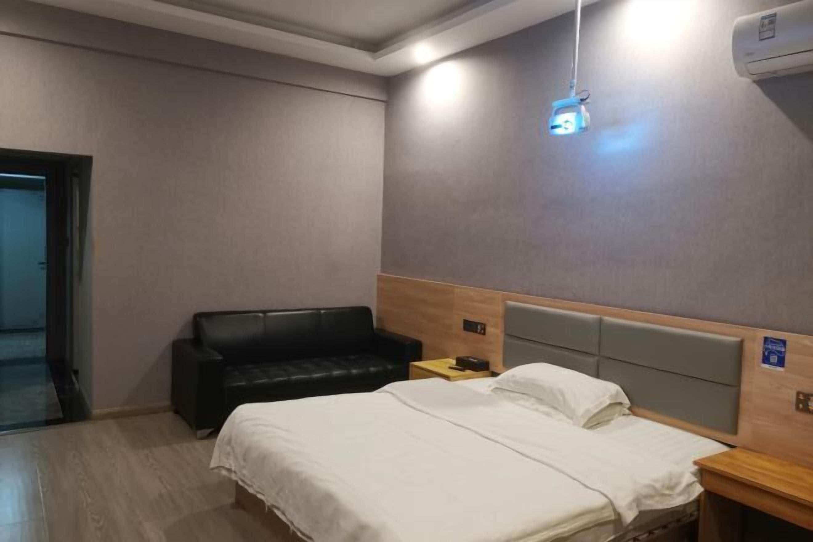 A hotel room with a bed, a black leather sofa, a bedside table, and a wall-mounted projector.