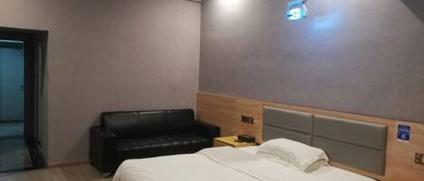 A hotel room with a bed, a black leather sofa, a bedside table, and a wall-mounted projector.