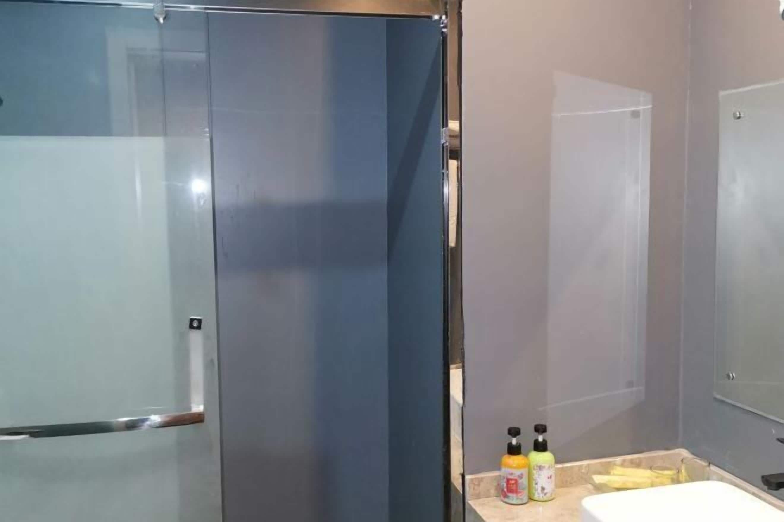 A bathroom with a glass shower enclosure, a sink, and two bottles of hand soap on the counter.