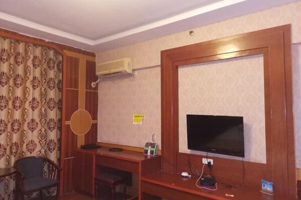 Une chambre d’hôtel avec un bureau en bois, une télévision, une chaise et un rideau à motifs.